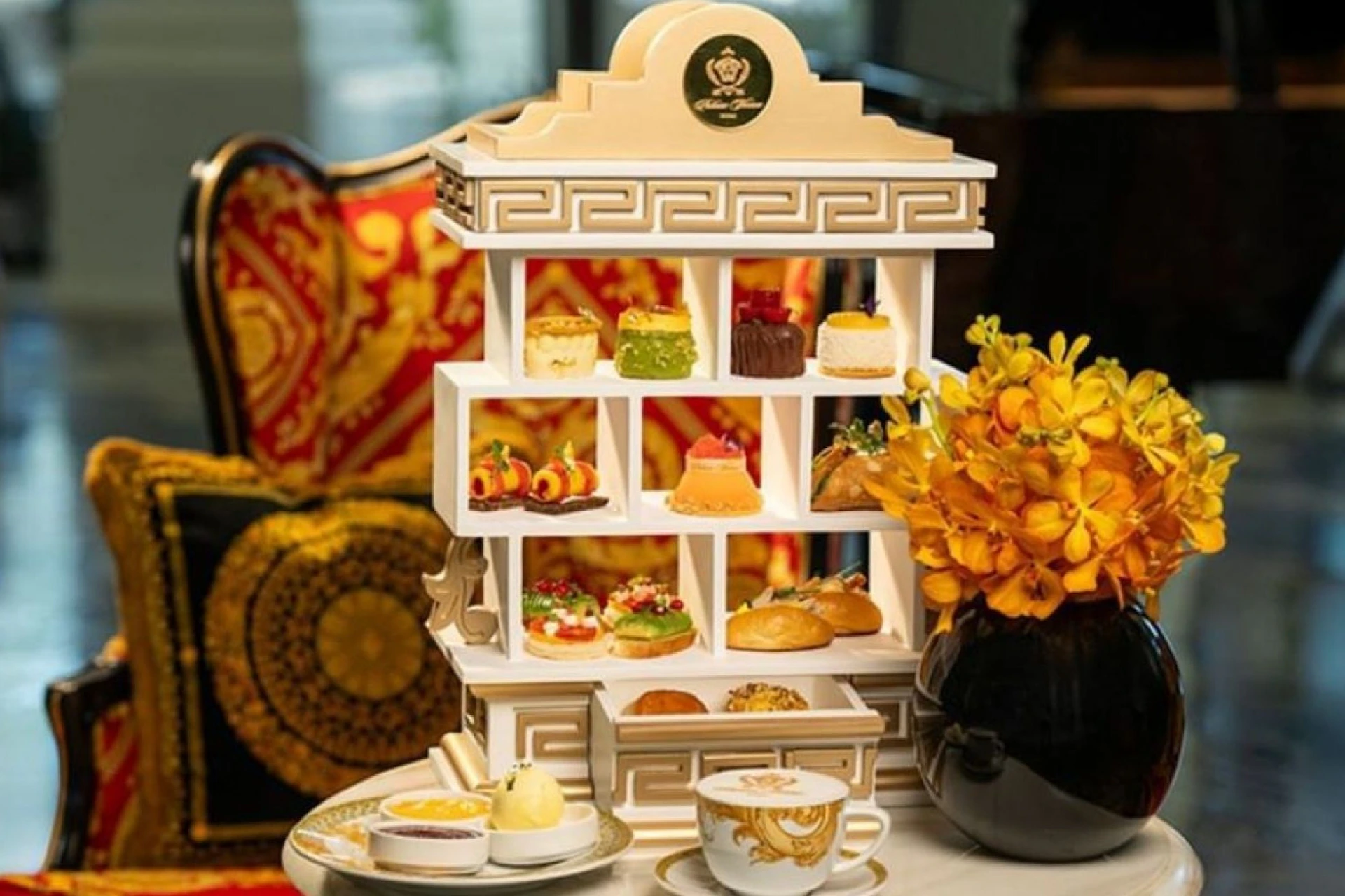 A luxurious afternoon tea set with tiered pastries, a cup of tea, and yellow flowers on a marble table.