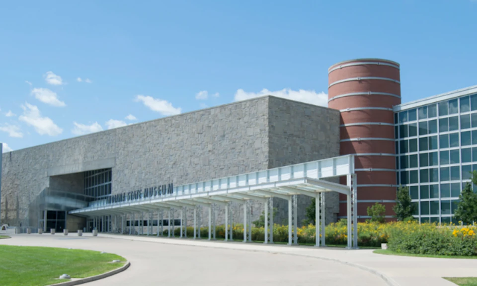 A modern building with a stone facade and a cylindrical red brick tower, featuring a covered pathway labeled "Indiana State Museum."