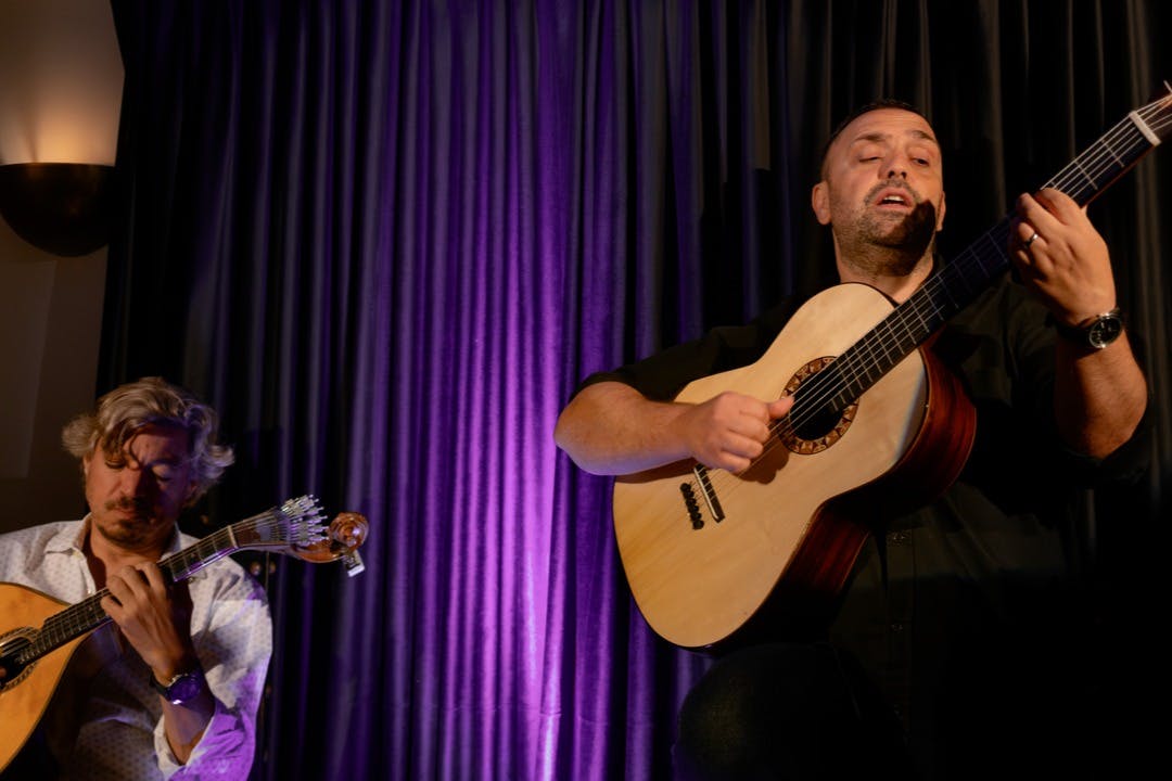 Lissabon-Konzerte - Zwei gitarrespielende Musiker auf der Bühne mit einem lila Vorhang im Hintergrund bei warmer Beleuchtung.