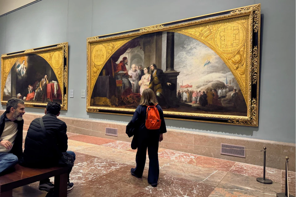 A visitor pauses in front of a grand altarpiece painting, framed by golden architectural elements.
