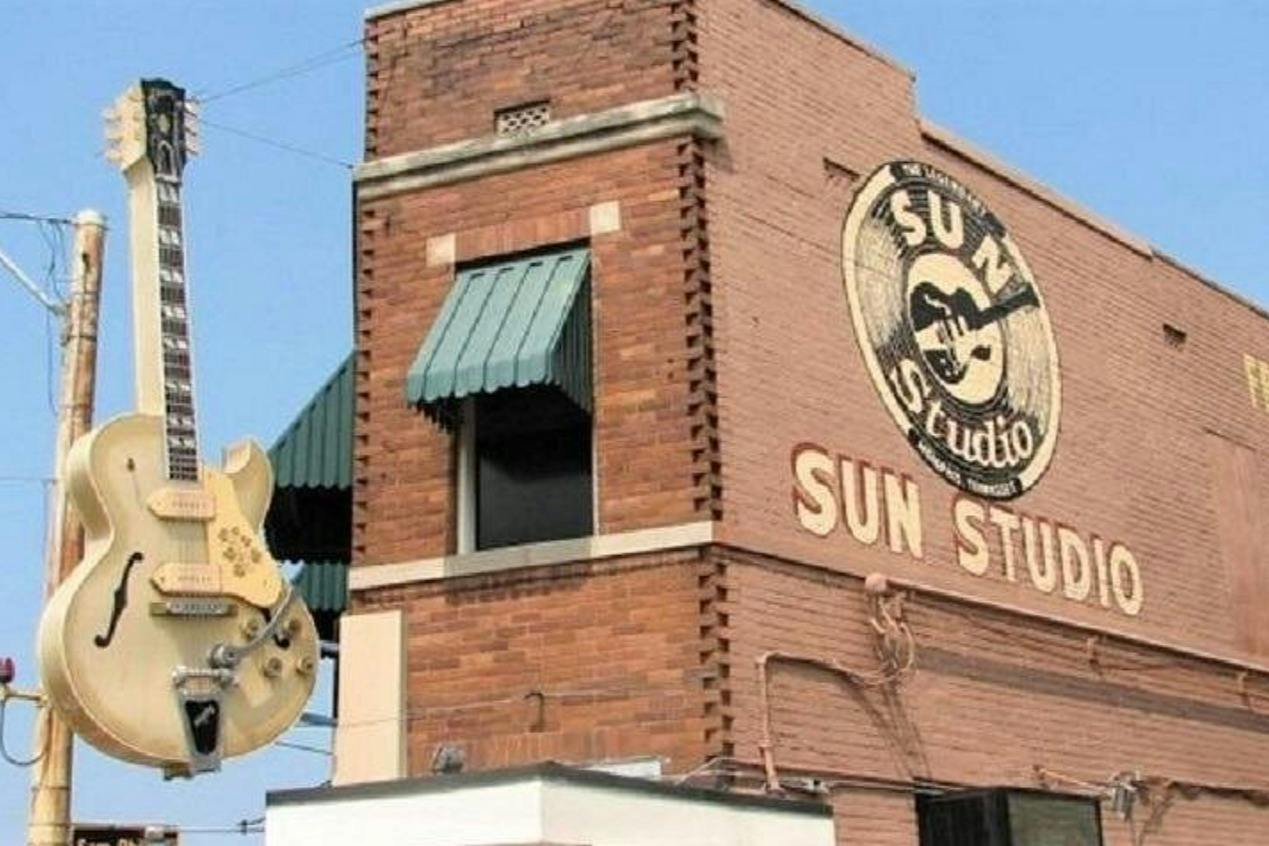 A brick building with a sign reading 'Sun Studio' and a painted guitar emblem, featuring a green window awning.