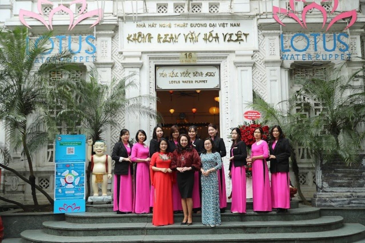 一群女性站在莲花水偶剧院入口前，她们大多穿着粉红色的传统礼服。