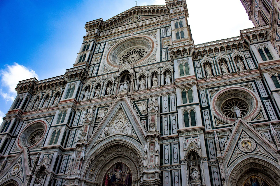 Intricate facade of a cathedral with ornate sculptures, rose windows, and detailed carvings under a blue sky.