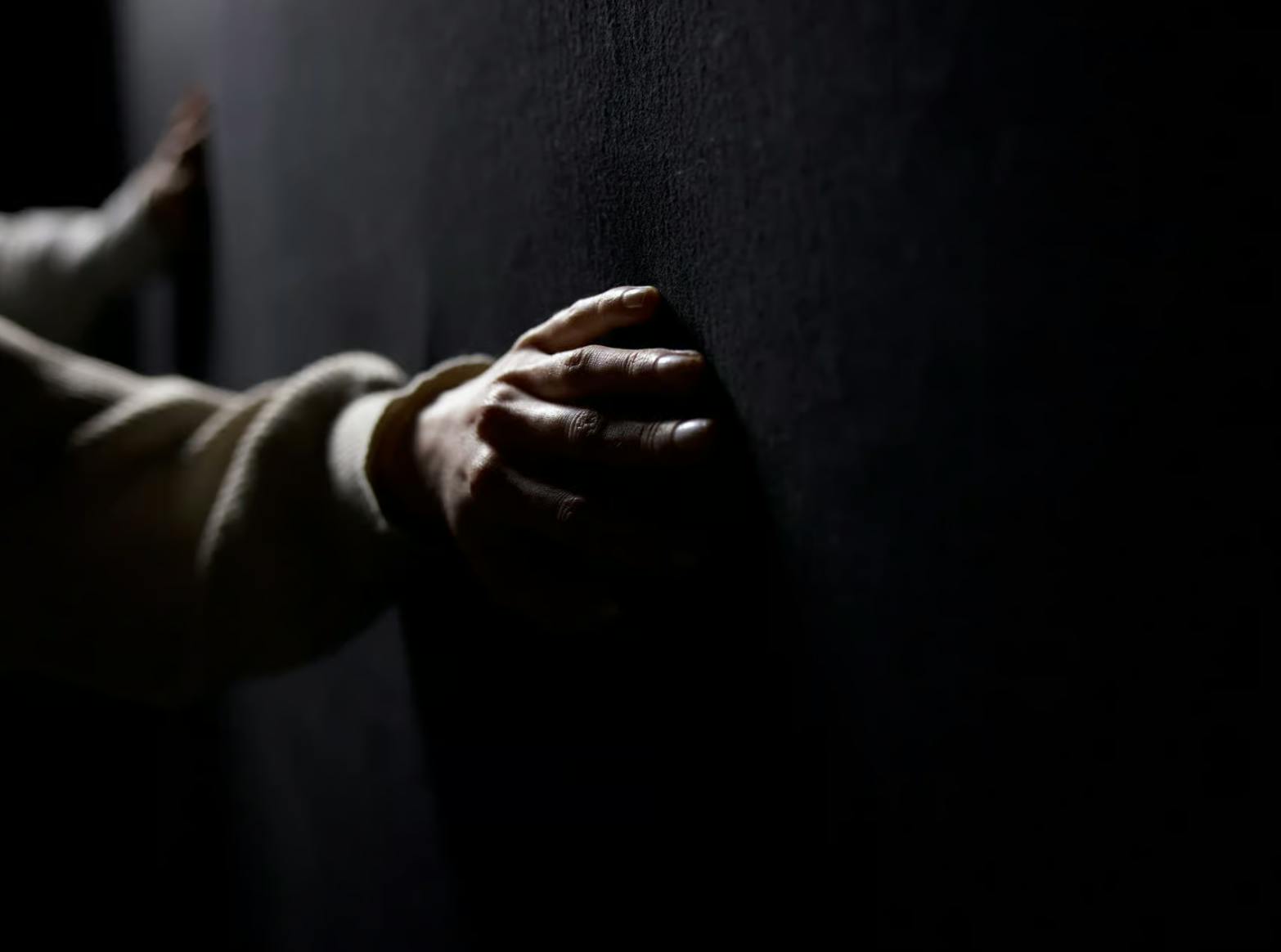 浅色袖子中的一只手在暗淡的光线下触摸黑暗的纹理墙壁。