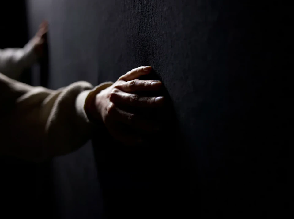 A hand in a light-colored sleeve touches a dark, textured wall in low lighting.