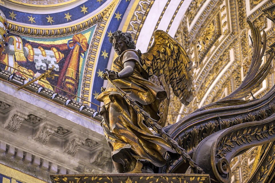 A golden angel statue with a sword, ornate surroundings, and a colorful mosaic ceiling in an elaborate interior.