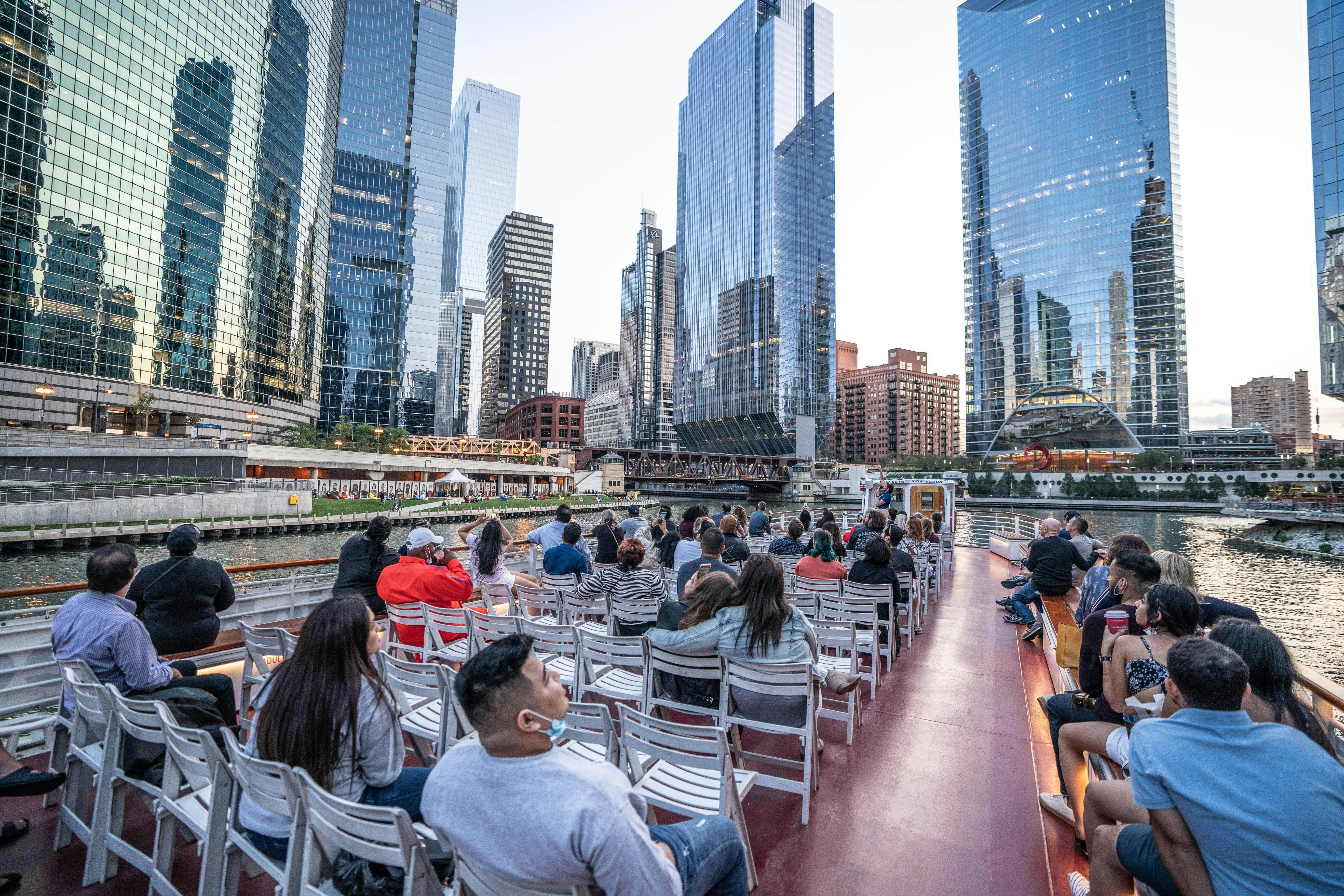 People seated on a boat tour, observing tall skyscrapers and buildings along a city river.