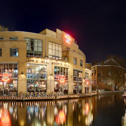 Ett Hard Rock Café upplyst på natten, beläget vid en kanal med en båt i närheten.