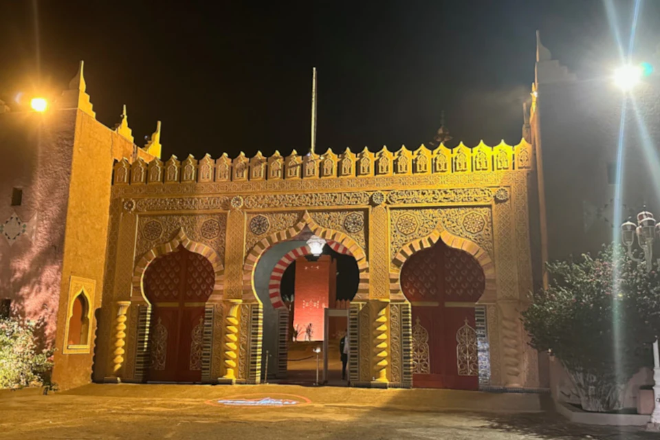 Ornate entrance gate with three arches, decorated with intricate patterns, lit up against a dark night sky.