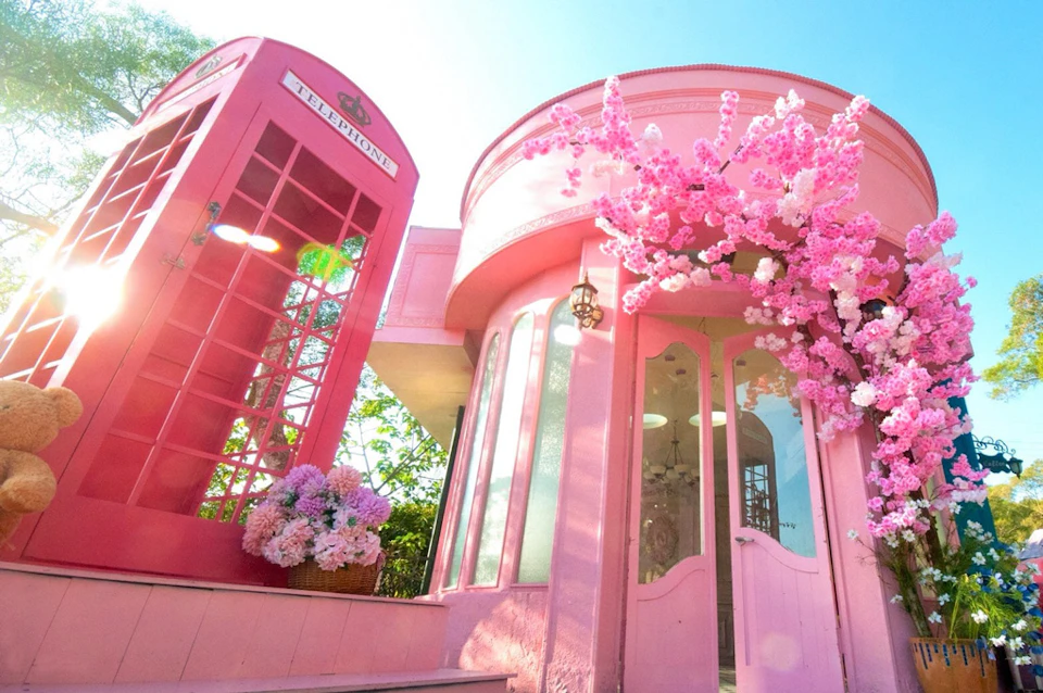 A pink building with a glass entrance, pink blossoms, and a pink phone booth with flowers outside.