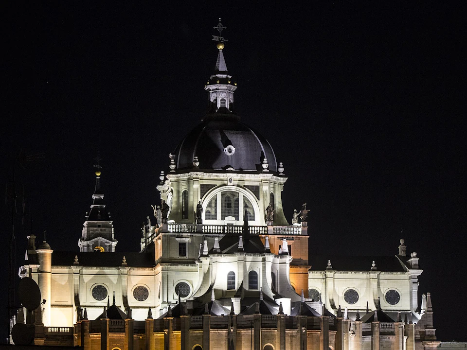 A large, illuminated cathedral with domes and statues on its roof against a dark night sky.