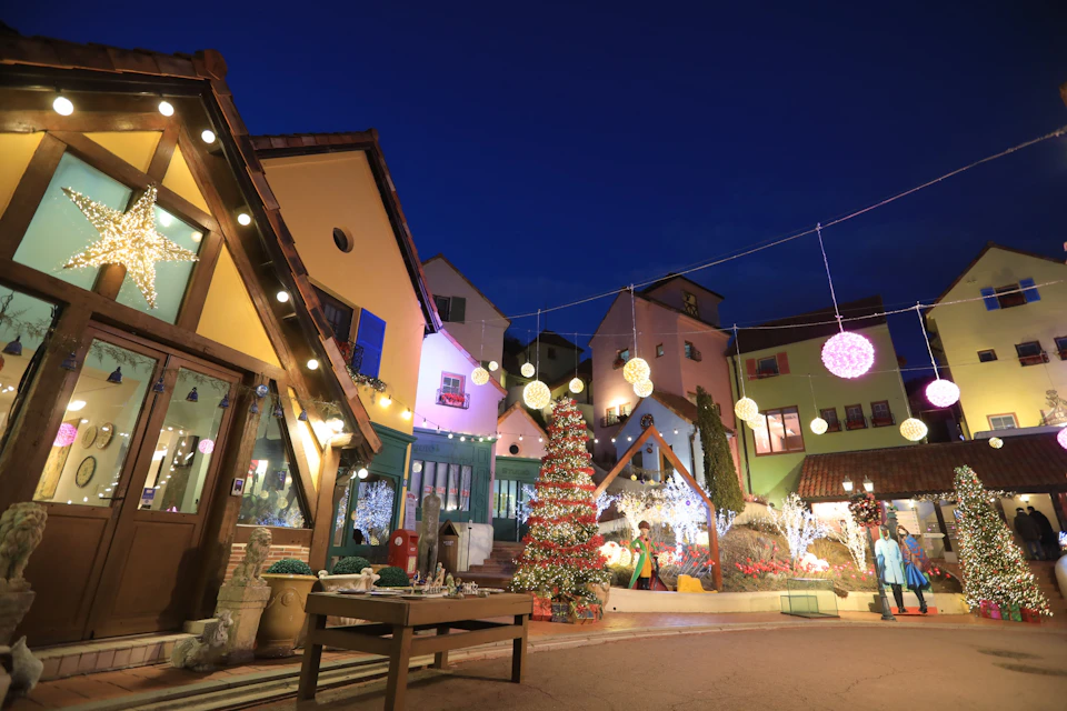 A festive courtyard at night with decorated houses, string lights, and a Christmas tree under a clear dark sky.