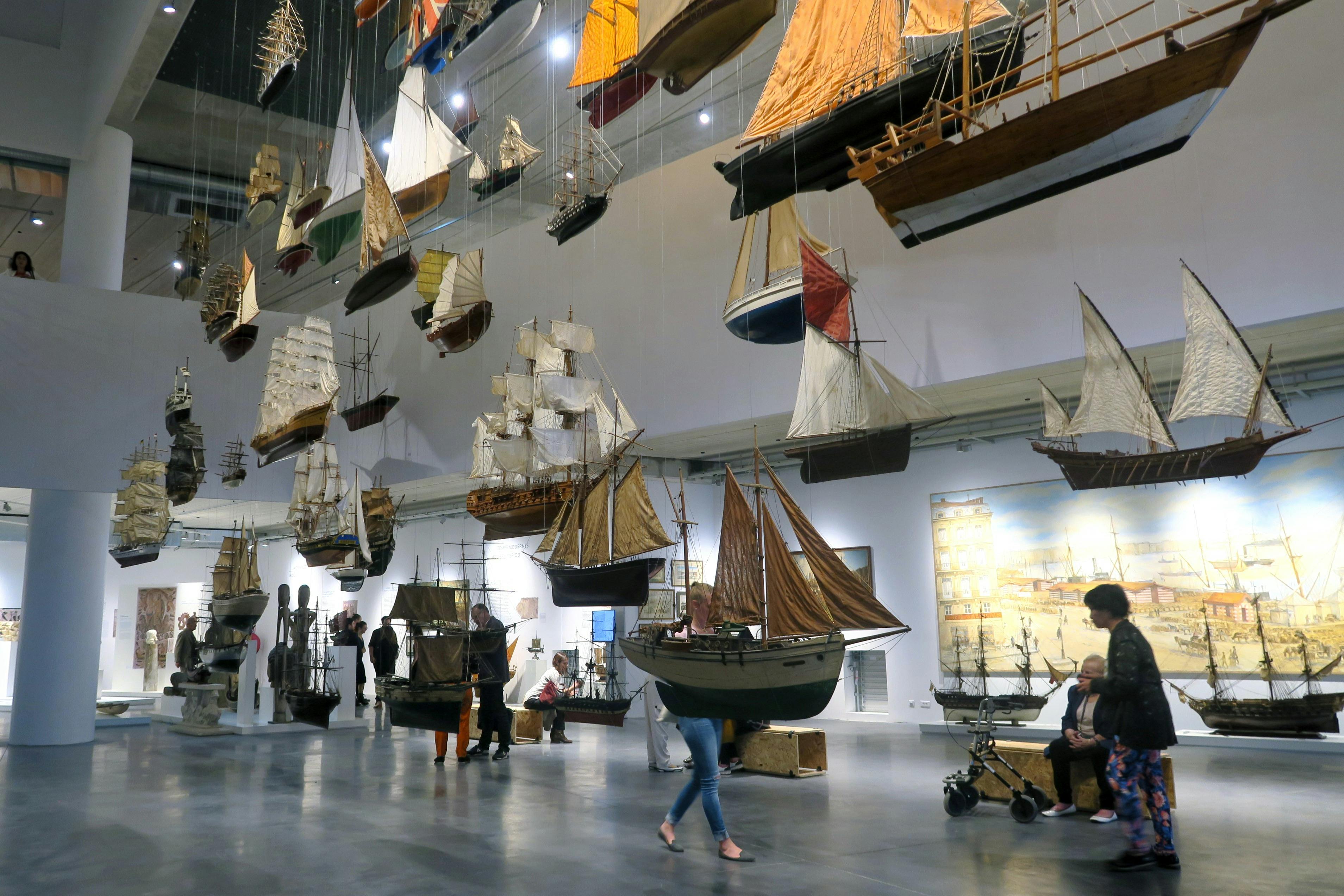 Museo che espone numerosi modelli di navi, con i visitatori che camminano e osservano le repliche dettagliate.