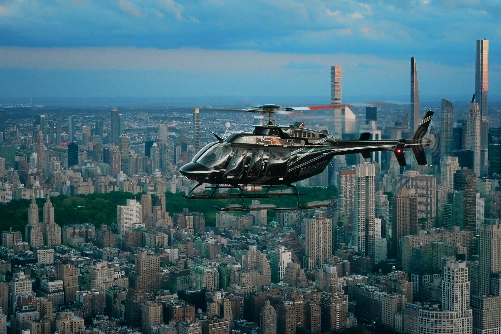 Um helicóptero preto sobrevoa uma paisagem urbana com edifícios densos e arranha-céus, sob um céu parcialmente nublado.