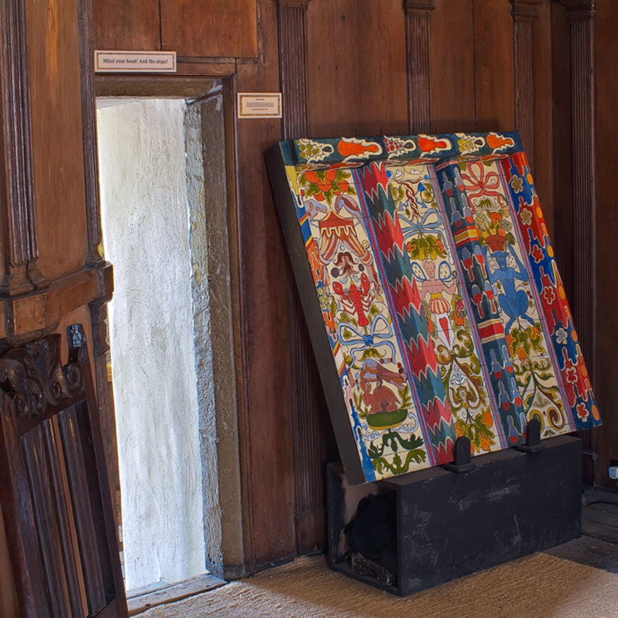 Una piccola porta strutturata accanto a un angolo che mostra pannelli di legno vibranti e intricati dipinti appoggiati alla parete.