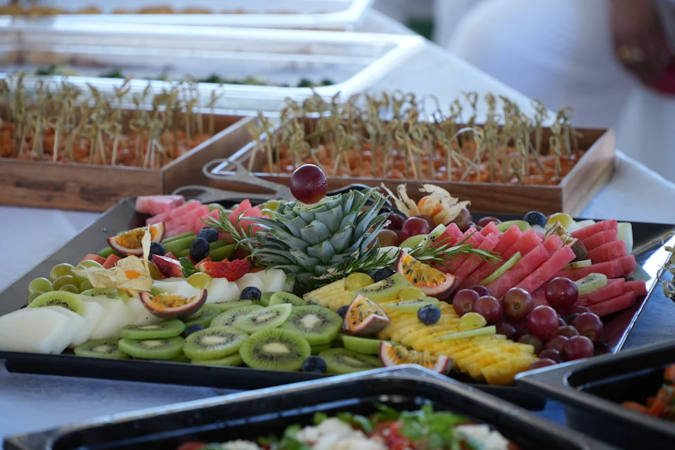 A colorful fruit platter featuring pineapple, kiwi, watermelon, grapes, and passion fruit, with sprouts in the background.
