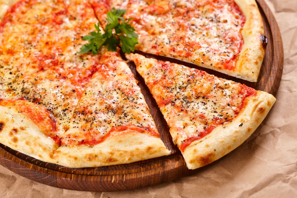 A freshly baked pizza with melted cheese, tomato sauce, herbs, and a garnish of parsley, served on a wooden board.