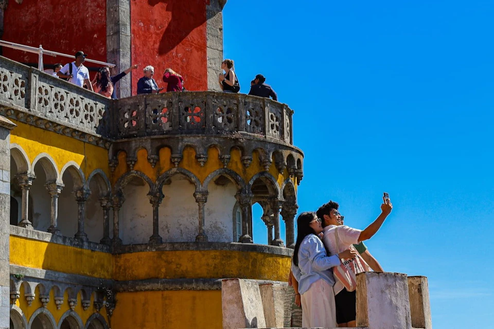A couple takes a selfie on a balcony of a colorful historical building under a clear blue sky.