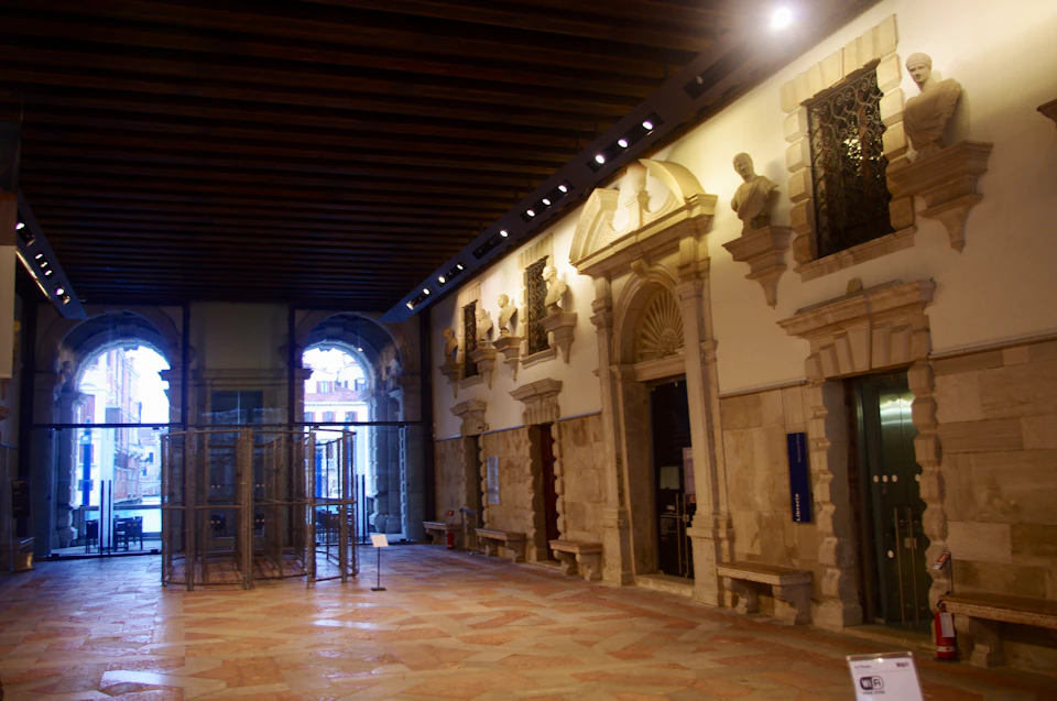 A spacious hallway with arched doorways, decorative stone architecture, and statues inside a historical building.