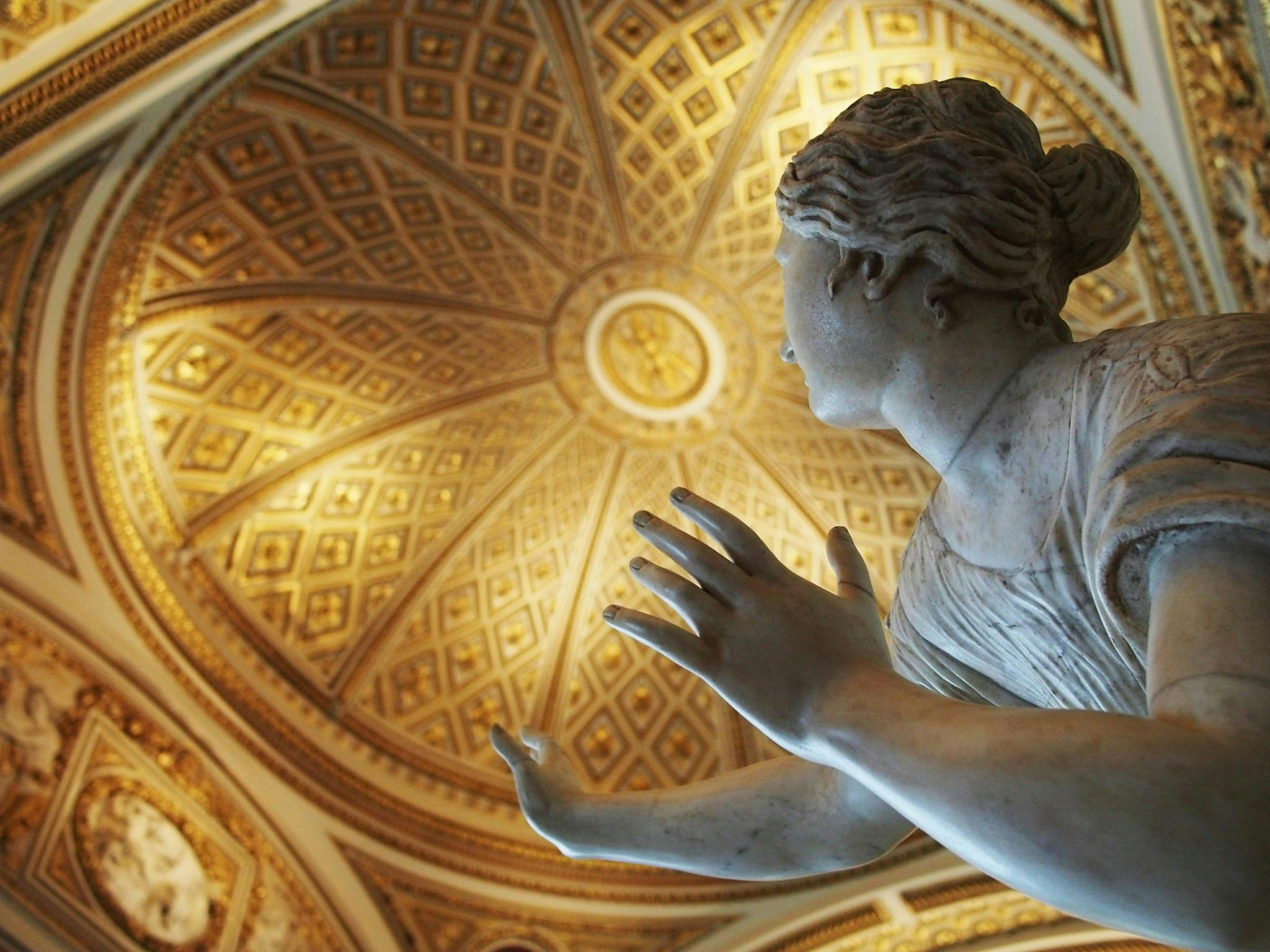 Marble statue of a woman in the foreground, against a backdrop of an ornate, gold-patterned domed ceiling.