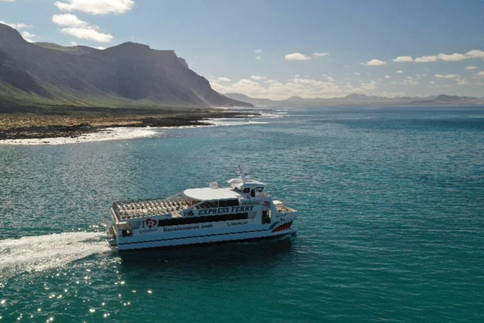 A white ferry boat labeled "EXPRESS FERRY" sails near a coastal mountain range under a partly cloudy sky.