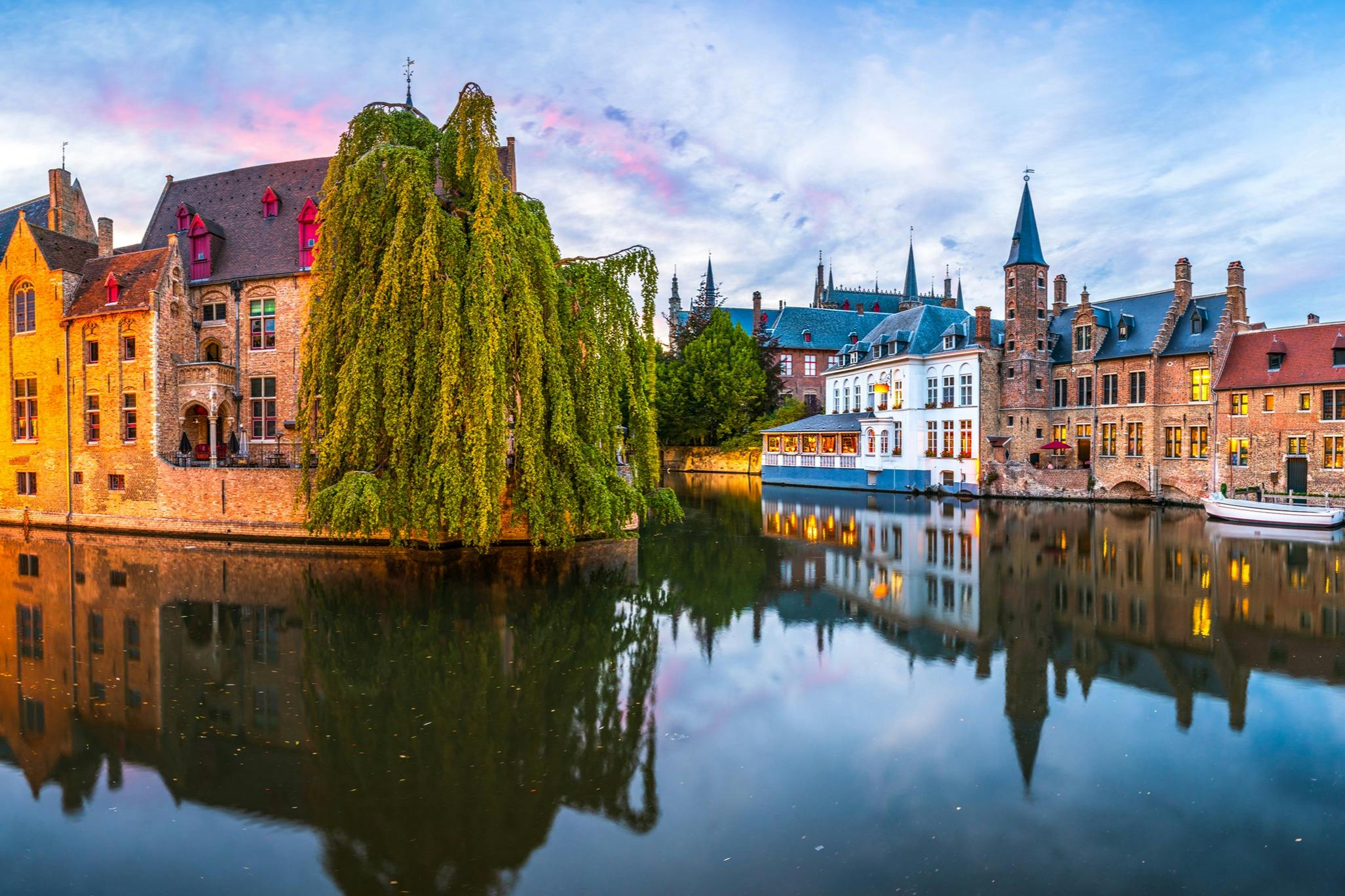 A serene canal scene with buildings reflected in the water, featuring a large weeping willow and picturesque architecture.