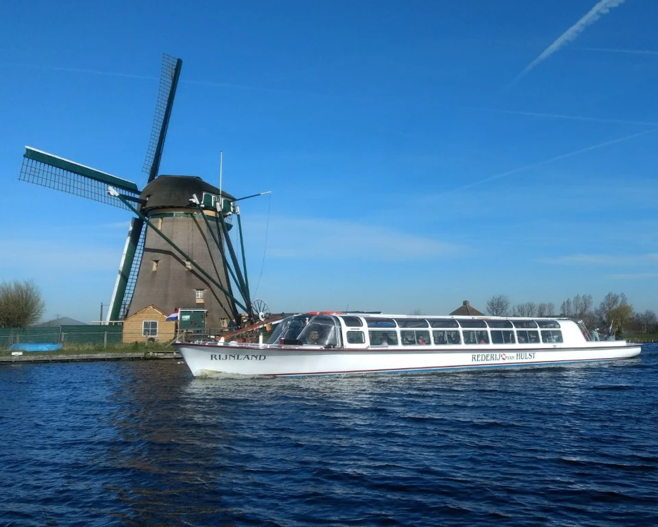 A boat passes by a traditional windmill on a clear day with a blue sky.