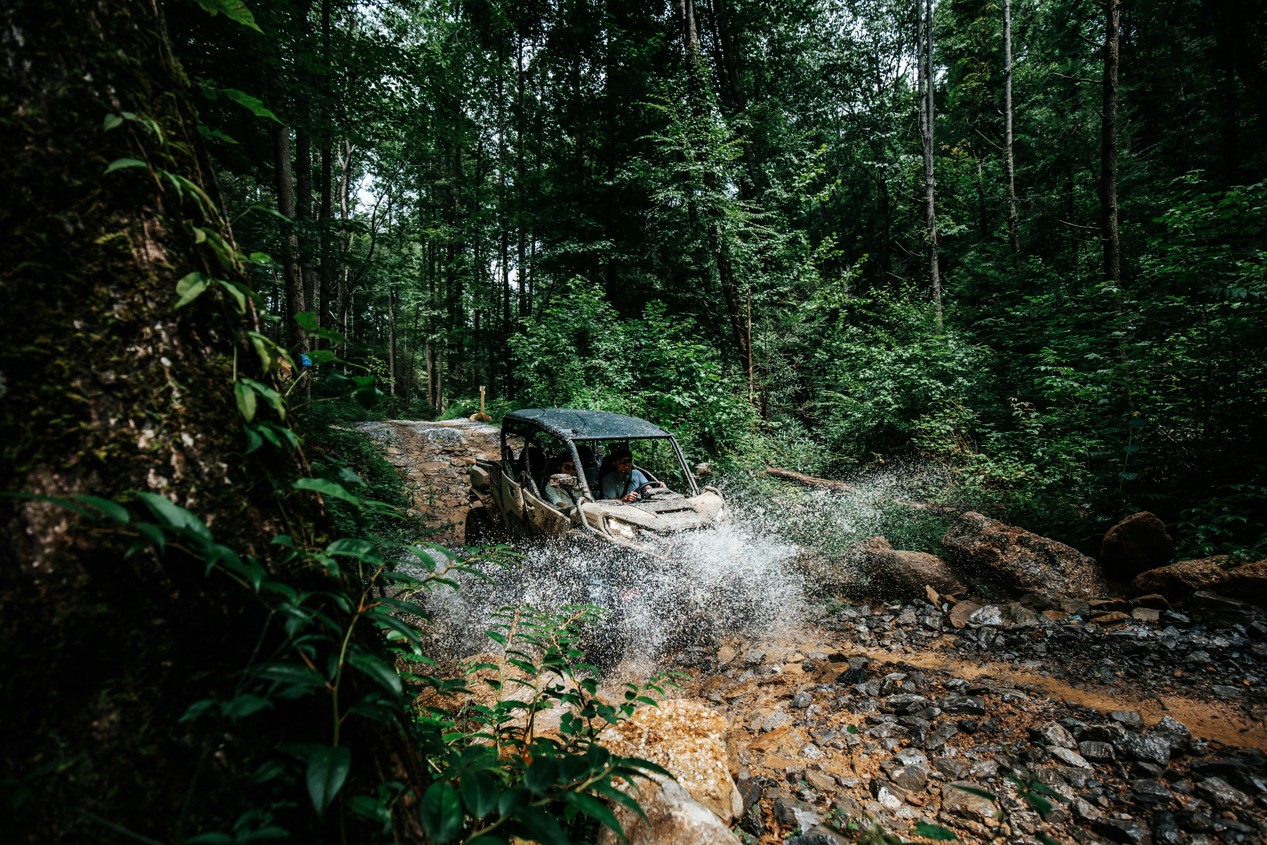 密林の中の泥だらけの水路を駆け抜け、水と泥を四方八方に飛ばしているユーティリティ車両。