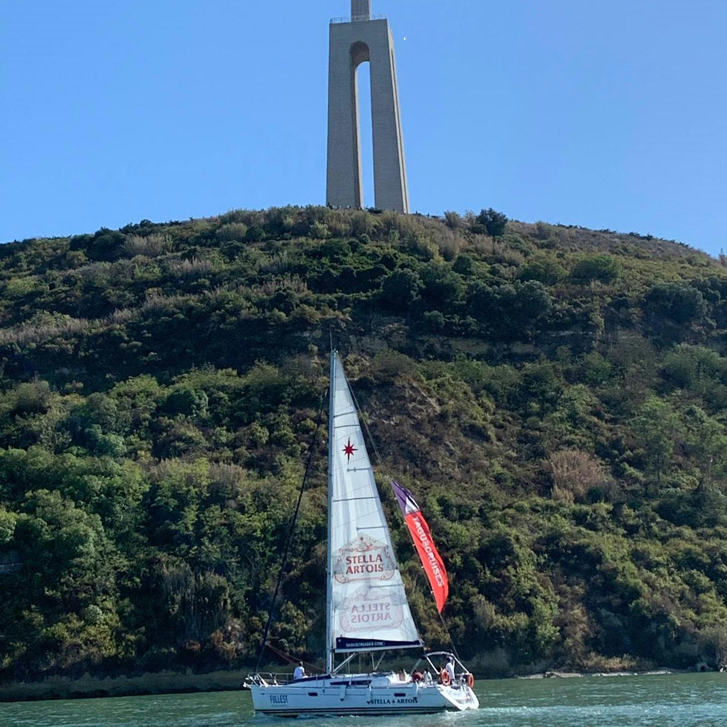 Una barca a vela sull'acqua con una collina e un alto monumento sullo sfondo, sotto un cielo azzurro e limpido.