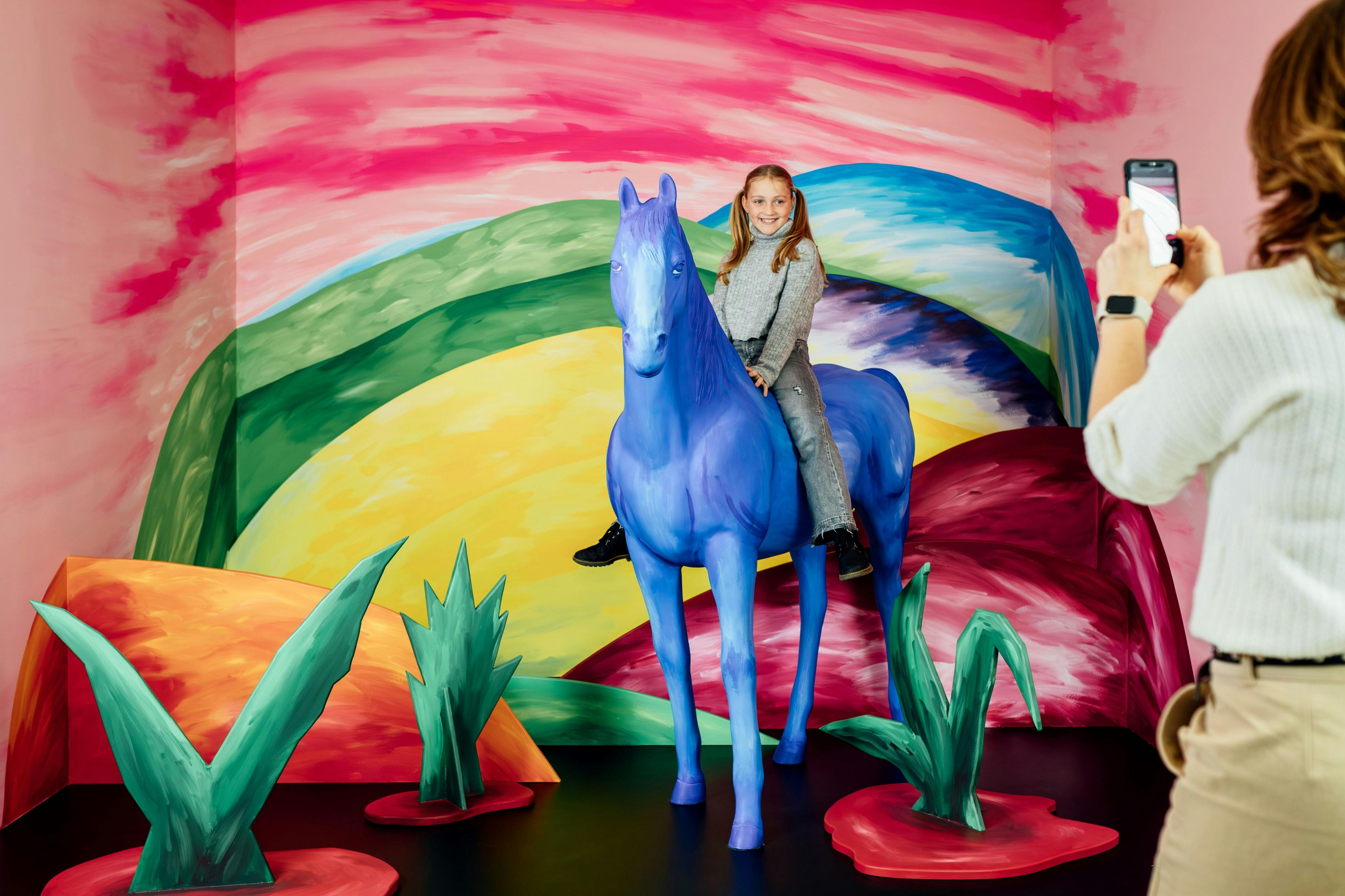 写真を撮られながら、カラフルな幻想的な風景の中で青い馬に乗ってポーズをとる子供– Magic Bavariの遊び心溢れる写真スポット
