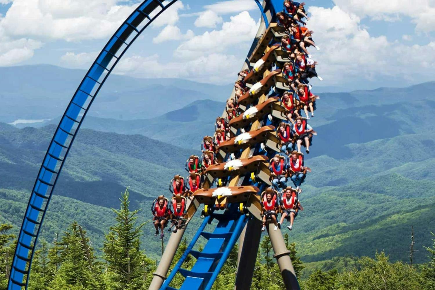 People riding a rollercoaster with a blue track in a mountainous landscape.