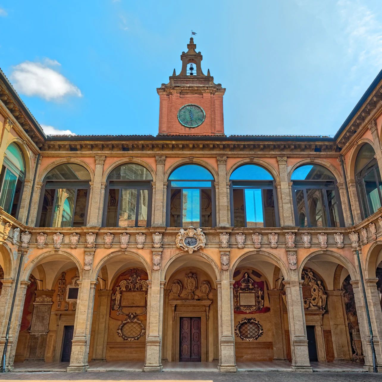 Historical building facade with arched windows, ornate columns, and a central clock tower under a blue sky.