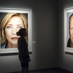 Person som tittar på stora porträtt av en kvinna och en man i ett svagt upplyst konstgalleri.