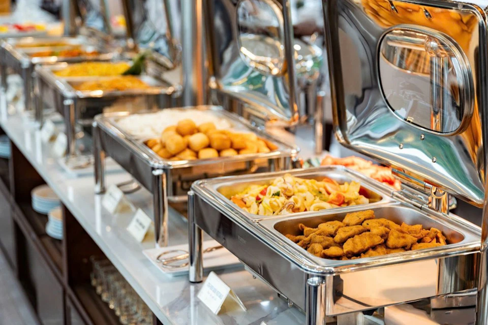 A buffet table with various dishes in stainless steel chafing dishes, including pasta, fried items, and other food.