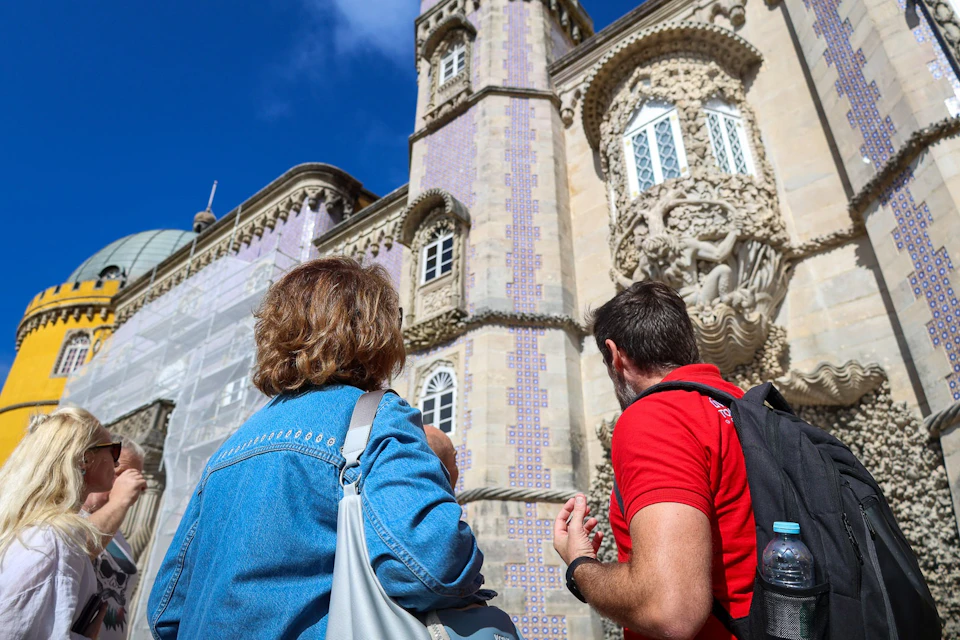 Two people admire a decorative building facade with intricate details and tiled patterns under a clear blue sky.