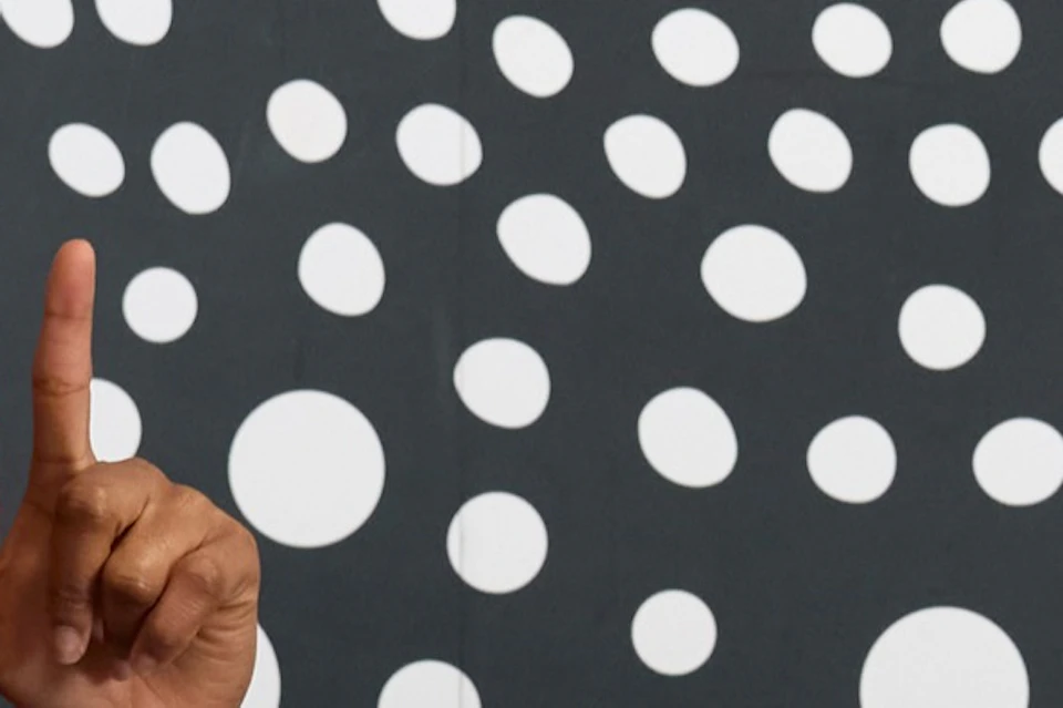 Two people are playing around in a room with a polka-dot pattern. One is wearing a spotted cloak, whilst the other is pointing at them.