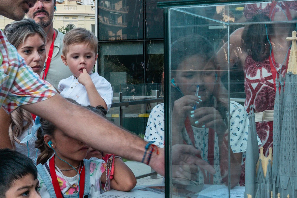A man shows a group of adults and children a model of a cathedral encased in glass.