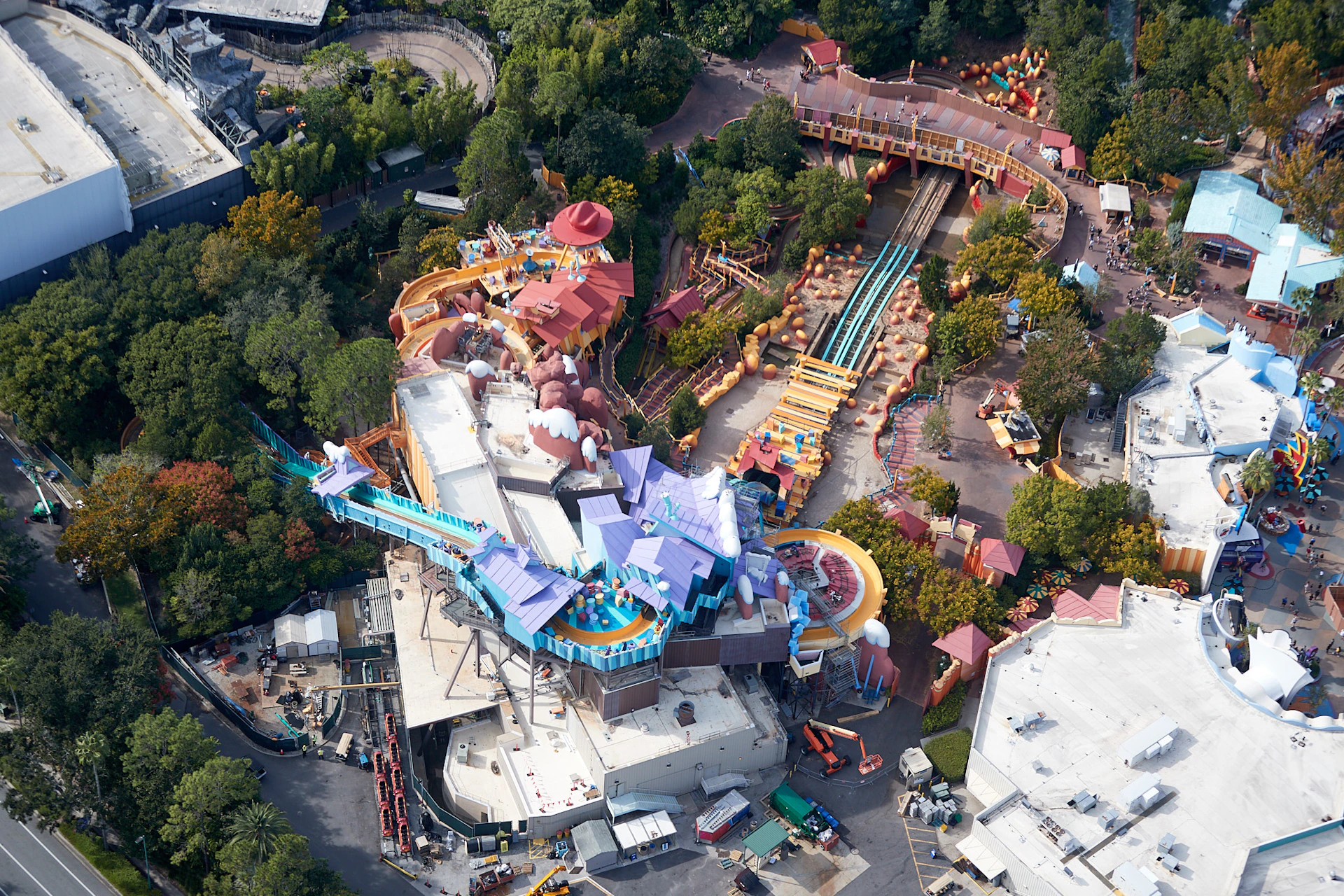 Aerial view of a colorful theme park attraction with water slides, tracks, and vibrant buildings surrounded by greenery.