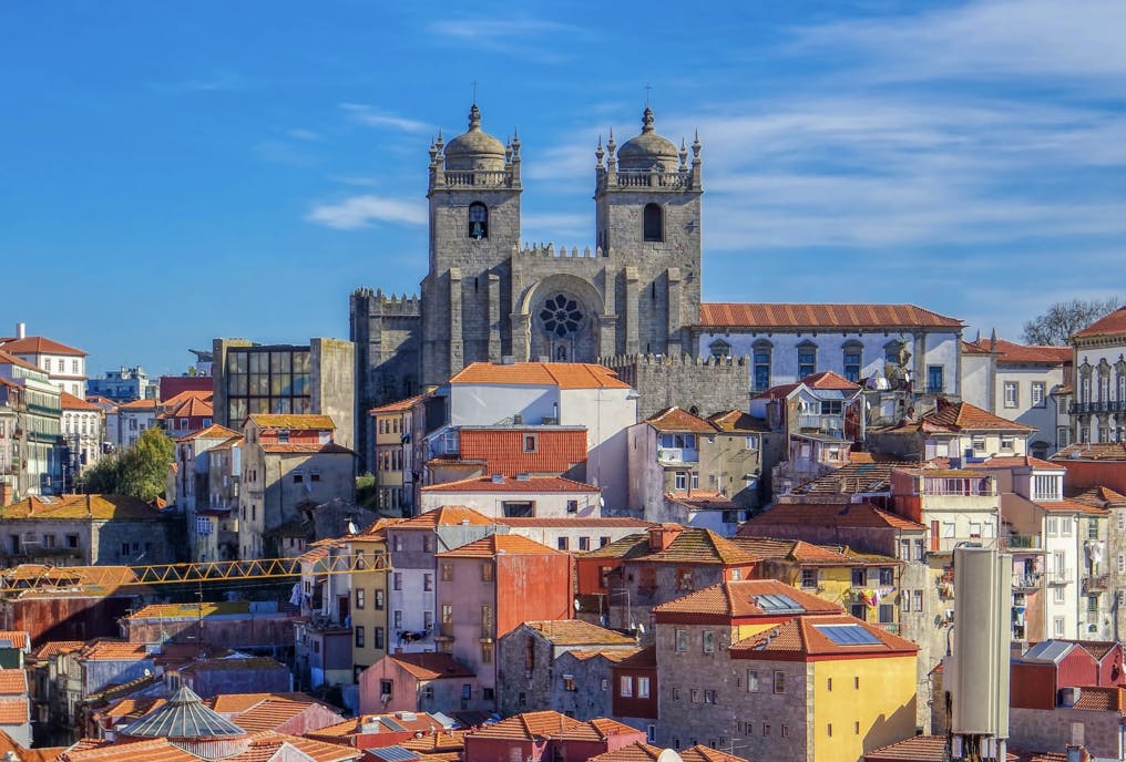 澄んだ青い空の下、赤いタイル張りの屋根を持つ密集した建物の上に建つ歴史的な大聖堂の塔。