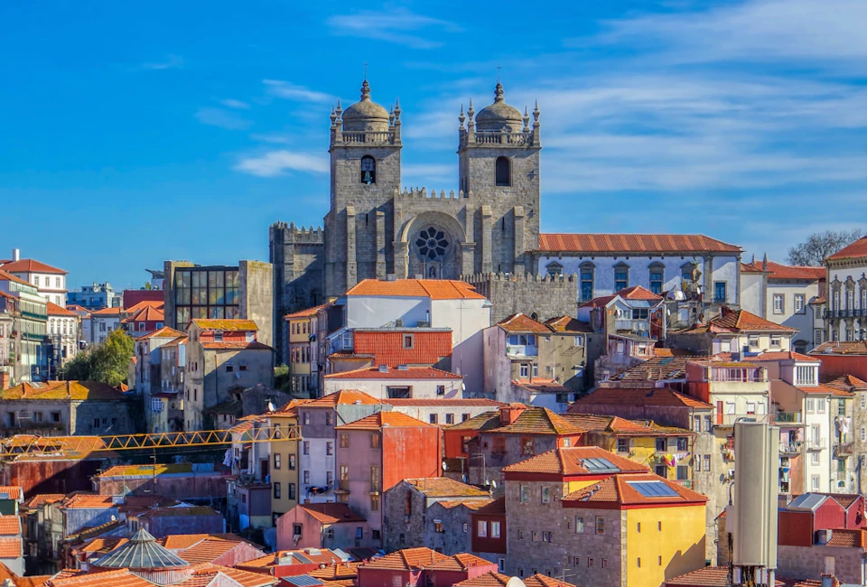 A historic cathedral towers over densely packed buildings with red-tiled roofs under a clear blue sky.