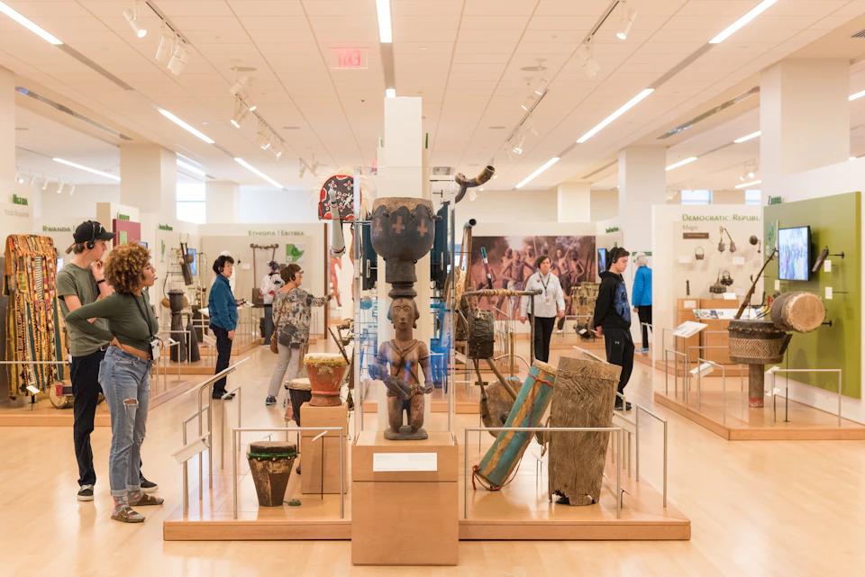 People exploring a spacious museum gallery filled with various cultural artifacts displayed in glass cases and on pedestals.