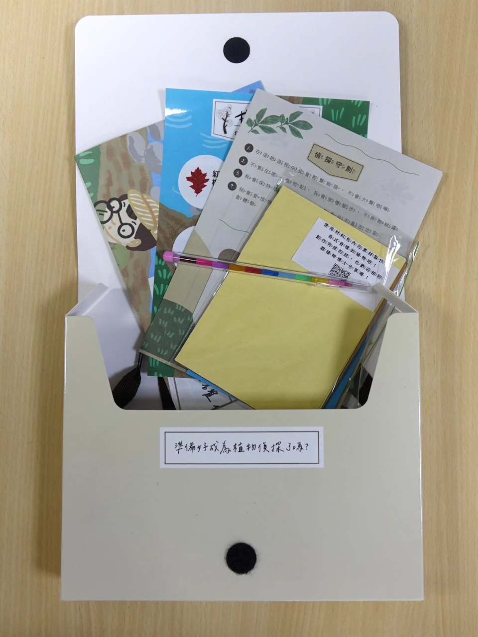 A folder containing various colorful papers, booklets, and a pen, placed on a wooden surface.