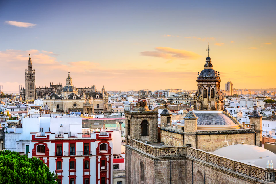 Cityscape view of Seville at sunset, featuring historic buildings, church towers, and a clear sky.