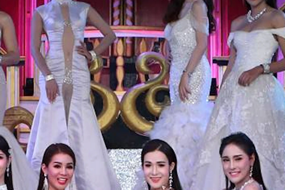 A group of women in elegant dresses posing on a stage with decorative backgrounds and lighting.