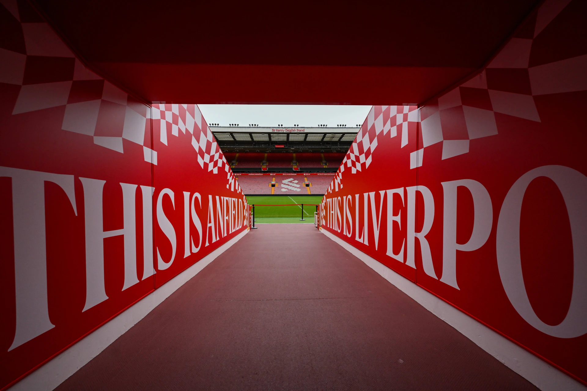 A tunnel leading to a football pitch with red walls displaying "This is Anfield" and a stadium visible beyond.