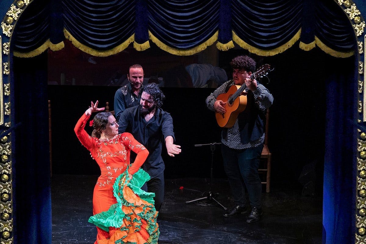 Uno spettacolo di flamenco con una ballerina in abito rosso, un chitarrista e due cantanti su un palco decorato con tende blu e oro.