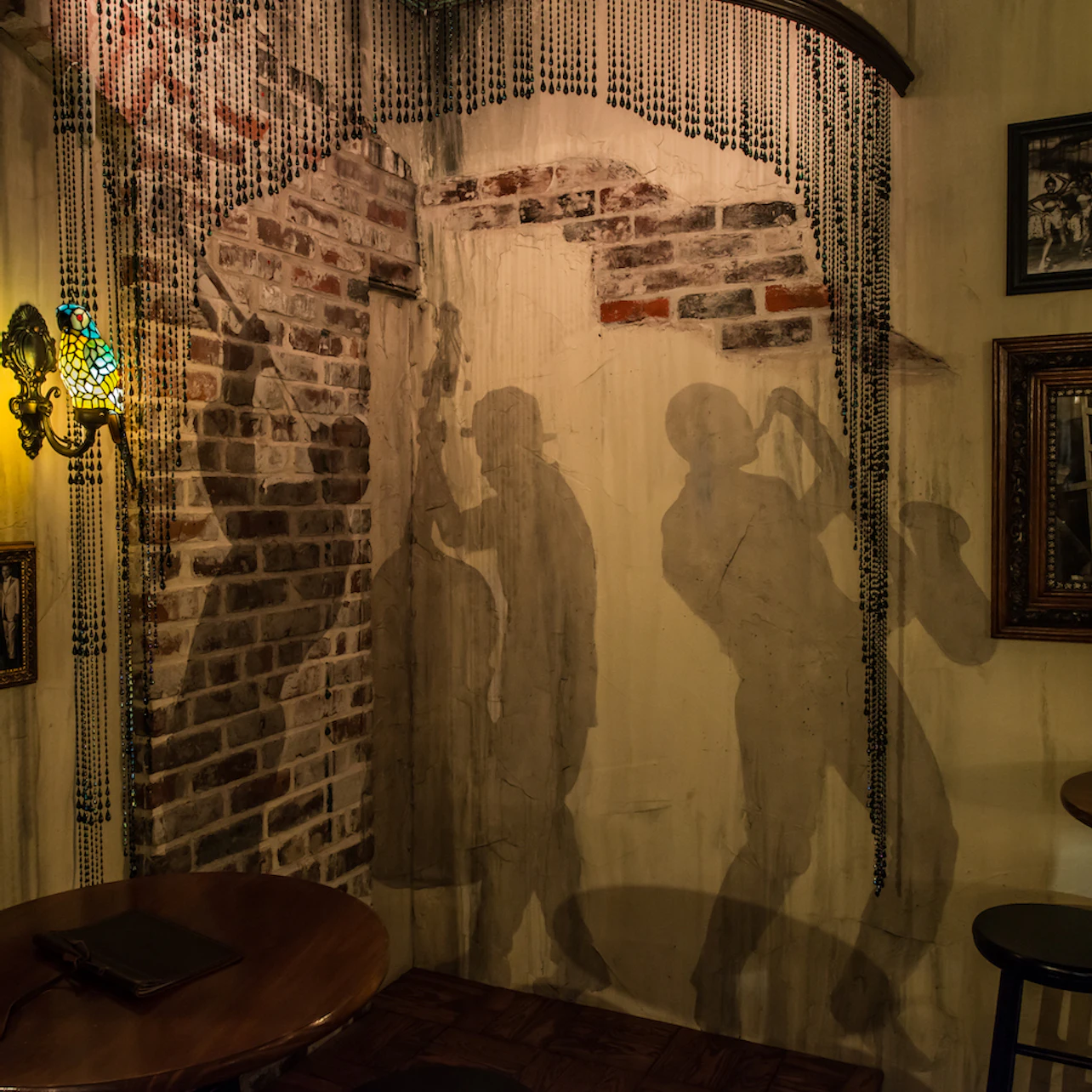 A dimly lit room with shadow murals of jazz musicians on a brick wall, adorned with beaded curtains and vintage decor.