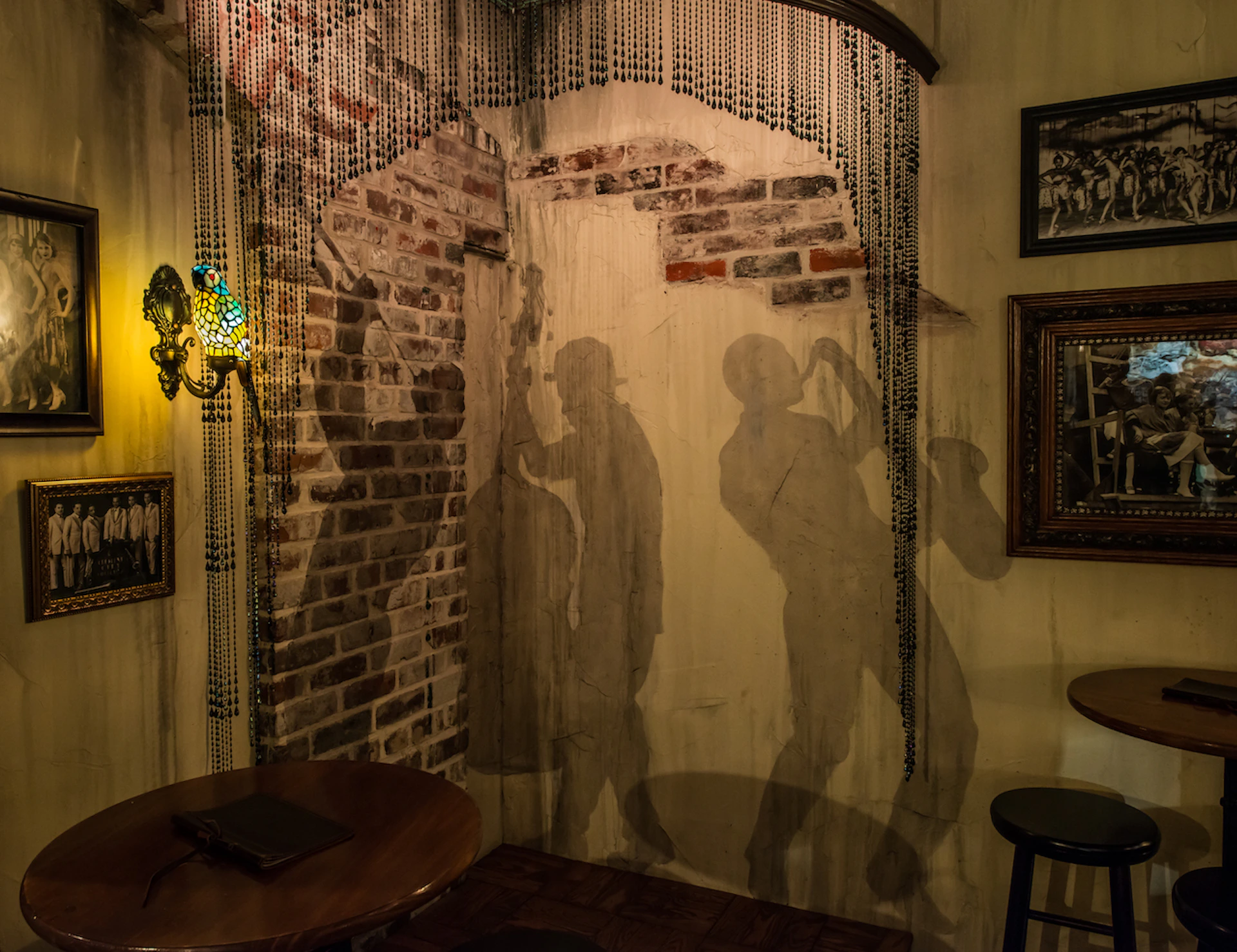 A dimly lit room with shadow murals of jazz musicians on a brick wall, adorned with beaded curtains and vintage decor.