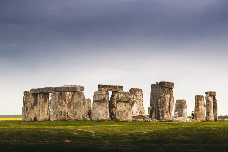 A view of Stonehenge under a cloudy sky, with its iconic stone structures standing on a grassy field.