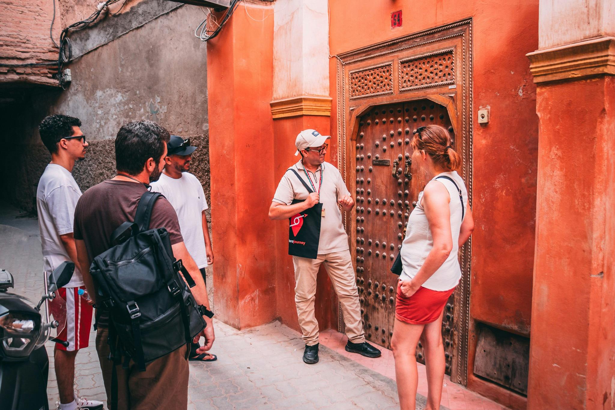 Un groupe de quatre hommes se tient devant une porte en bois ornée, dans une ruelle étroite. L'un d'entre eux montre du doigt et explique quelque chose.